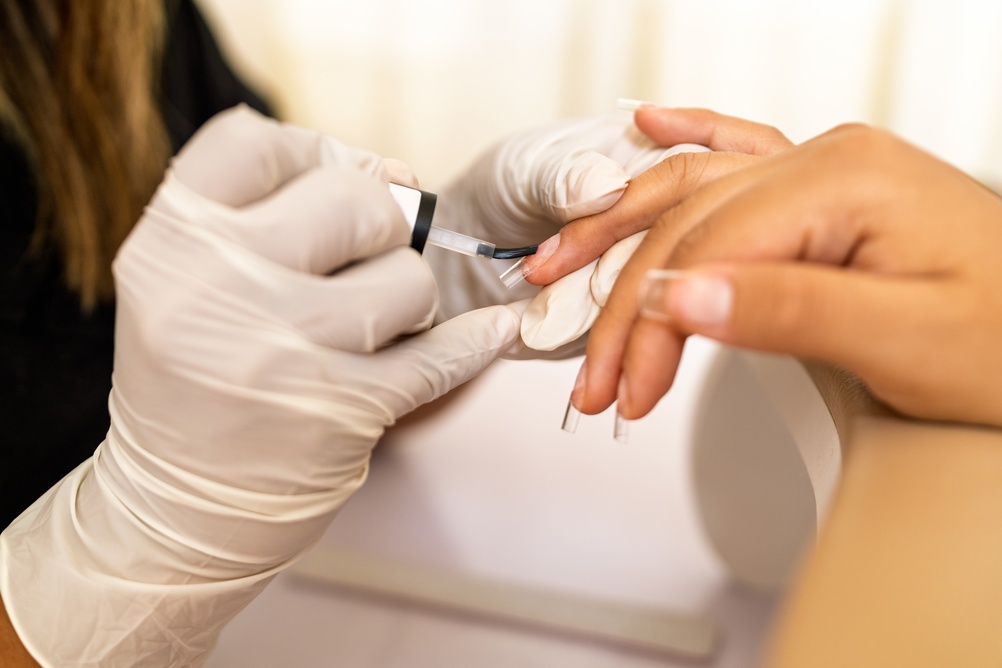 professional,manicurist,in,gloves,applying,clear,nail,polish,to,client's